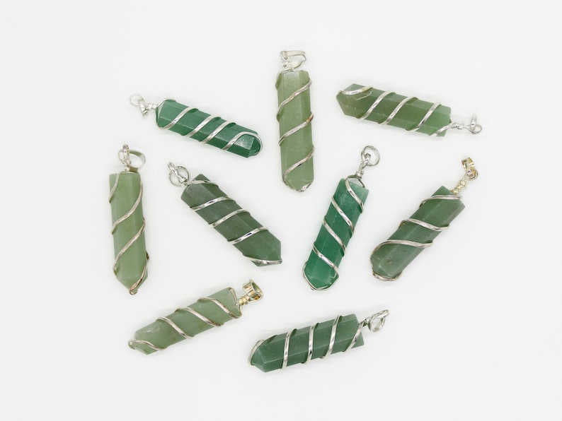May include: A collection of green gemstone pendants with silver wire wrapping. Each pendant is a hexagonal shape with a loop at the top for a chain. The pendants vary slightly in shade, from light to dark green.