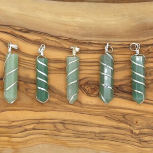 May include: Six green gemstone pendants with silver wire wrapping are displayed on a wooden surface. Each pendant has a hexagonal shape and a silver loop at the top for hanging. The pendants vary slightly in shade of green.