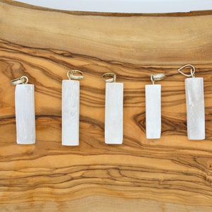 May include: Six white selenite crystal pendants of varying sizes, displayed on a wooden surface.