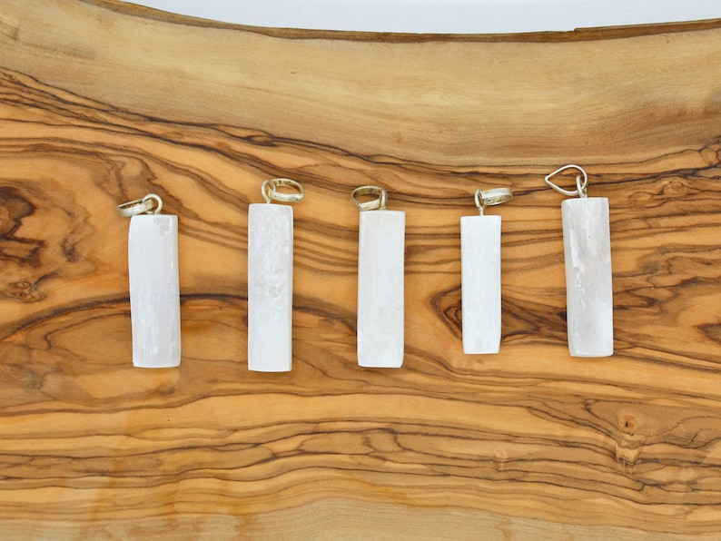 May include: Six white selenite crystal pendants of varying sizes, displayed on a wooden surface.