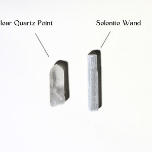 May include: A clear quartz point and a selenite wand, both white crystals, are displayed on a white surface. The text "Clear Quartz Point" is above the quartz point and the text "Selenite Wand" is above the wand.