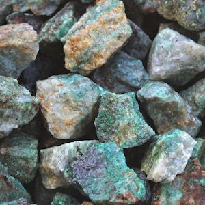 May include: A collection of rough, raw, green and white malachite stones. The stones are various sizes and shapes.