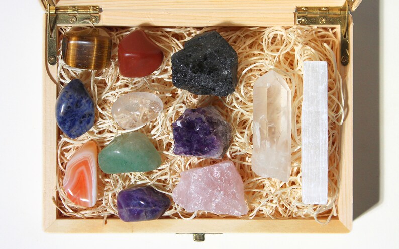 May include: A wooden box filled with a variety of crystals and stones, including amethyst, rose quartz, clear quartz, tiger's eye, and selenite.