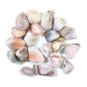 May include: A collection of tumbled agate stones in various shades of pink, white, and gray. The stones have a smooth, polished surface and are arranged in a circular pattern.