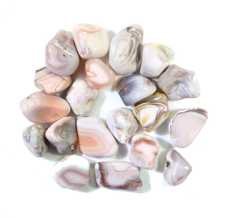 May include: A collection of tumbled agate stones in various shades of pink, white, and gray. The stones have a smooth, polished surface and are arranged in a circular pattern.