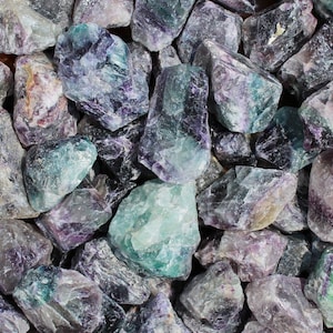 May include: A close-up view of a collection of green and purple fluorite crystals. The crystals are rough and have a variety of shapes and sizes.