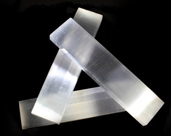 May include: Three selenite wands, also known as satin spar, are arranged in a triangular shape against a black background. The wands are translucent and have a smooth, polished surface.