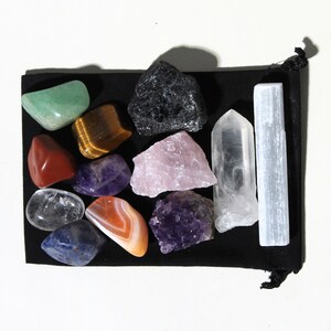 May include: A collection of 13 crystals and stones in a black velvet pouch. The crystals include amethyst, rose quartz, clear quartz, tiger's eye, selenite, red jasper, green aventurine, blue lace agate, and obsidian.