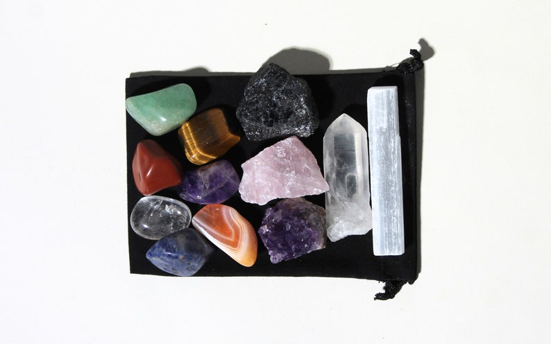 May include: A collection of 13 crystals and stones in a black velvet pouch. The crystals include amethyst, rose quartz, clear quartz, tiger's eye, selenite, red jasper, green aventurine, blue lace agate, and obsidian.