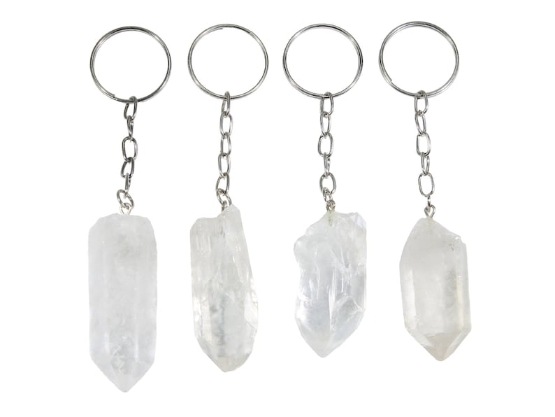 May include: Four clear quartz crystal keychains. Each keychain features a raw, natural quartz crystal pendant attached to a silver-tone chain and keyring. The crystals vary slightly in shape and size, showcasing their unique, natural formations.