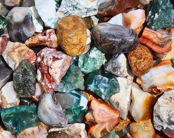 May include: A collection of polished gemstones in various colors, including green, orange, white, and brown. The stones have unique patterns and textures, with some displaying bands and swirls. The gemstones are likely used for jewelry or decorative purposes.