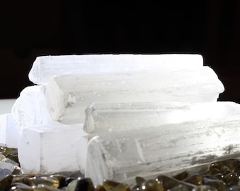 May include: A pile of white selenite crystal sticks, also known as satin spar, on a bed of brown and clear glass stones.