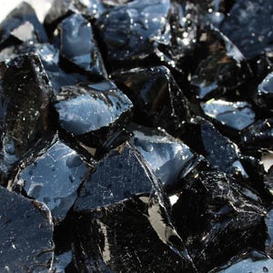 Puede incluir: Primer plano de un mont&oacute;n de rocas de obsidiana negras y brillantes. Las rocas tienen formas irregulares y reflejan la luz, creando una apariencia brillante. Las piezas de obsidiana var&iacute;an en tama&ntilde;o y est&aacute;n agrupadas.