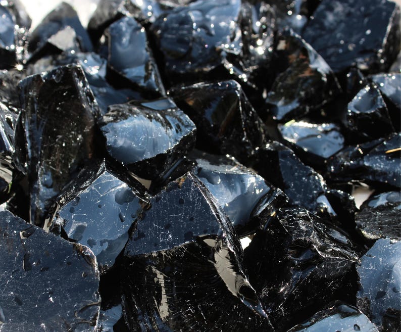 Puede incluir: Primer plano de un mont&oacute;n de rocas de obsidiana negras y brillantes. Las rocas tienen formas irregulares y reflejan la luz, creando una apariencia brillante. Las piezas de obsidiana var&iacute;an en tama&ntilde;o y est&aacute;n agrupadas.