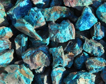 May include: A close-up of a pile of rough, raw turquoise stones. The stones are a vibrant blue-green color with brown and black markings.