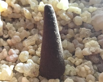 May include: A brown incense cone resting on a bed of white and yellow resin crystals.