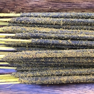 Puede incluir: Primer plano de un paquete de varillas de incienso. Las varillas son negras con un revestimiento amarillo y tienen una textura rugosa.