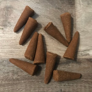 Pode incluir: Uma coleção de dez cones de incenso marrons. Os cones estão dispostos em forma de estrela sobre uma superfície de madeira.