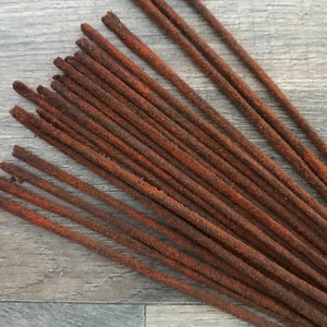 May include: A collection of incense sticks with a textured, reddish-brown appearance. The sticks are arranged in a slightly overlapping pattern, showcasing their rustic and natural aesthetic. The incense sticks are a warm, earthy tone.