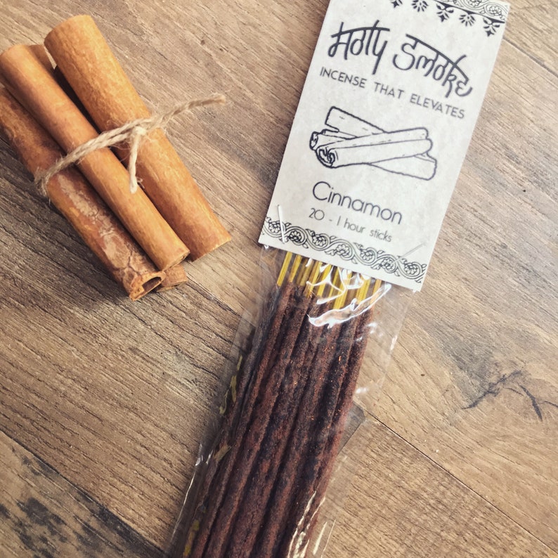 May include: A bundle of cinnamon sticks tied with twine next to a package of incense sticks. The incense package reads "Holy Smoke" and "Cinnamon" with 20 one-hour sticks.