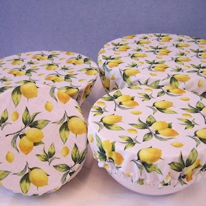 May include: Set of four reusable food covers with a lemon print. The covers are made of fabric and have a white background with yellow lemons and green leaves.