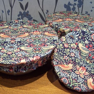 May include: Three round fabric covers with a floral pattern in shades of blue, green, yellow, and pink. The covers have a ruffled edge and are made of a soft, cotton fabric.