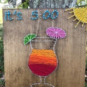 May include: A wooden sign with string art depicting a cocktail with a lime wedge and a pink umbrella. The sign reads "It's 5:00 Somewhere".