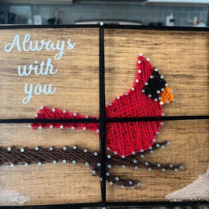 May include: A wooden sign with a red cardinal bird made of string art. The sign says "Always with you".