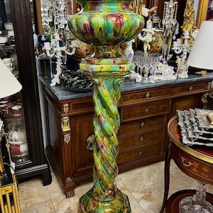 Könnte beinhalten: Ein hoher Keramiksockel mit einer spiralförmigen Säule und einer breiten, schalenförmigen Oberseite. Das Stück ist mit einer glänzenden, mehrfarbigen Glasur in leuchtenden Grün-, Gelb- und tiefen Rottönen versehen, die einen marmorierten Effekt erzeugt.