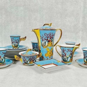 May include: A complete porcelain tea set with a marine theme. The set includes cups, saucers, plates, a teapot, a sugar bowl, and an ashtray. The pieces are light blue with coral and seashell designs, accented with gold.