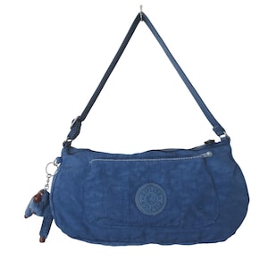 May include: A navy blue shoulder bag with a long strap. The bag has a zippered pocket on the front and a small, round logo patch. A small, blue monkey keychain hangs from the side. The bag is made of a lightweight, possibly nylon material.