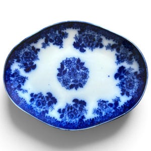 May include: An oval-shaped ceramic platter featuring a white base with a deep blue floral pattern. The design includes a central cluster of flowers surrounded by smaller floral arrangements along the scalloped rim, creating a high-contrast look.