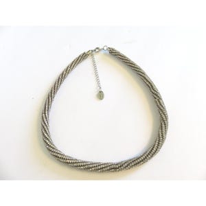 May include: Silver-toned necklace with a twisted rope design. The necklace features a series of small, sparkling embellishments, creating a shimmering effect. The adjustable chain and clasp are visible. The jewelry is set against a white background.
