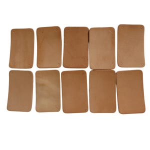 May include: Ten rectangular, light brown leather pieces arranged in two rows. Each piece has rounded corners and small, evenly spaced holes. The leather has a natural, slightly textured appearance.