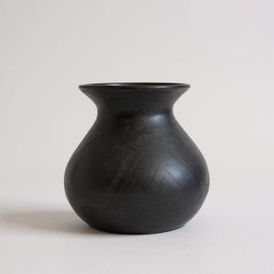 May include: A black ceramic vase with a rounded body and a slightly flared rim. The vase has a matte finish and subtle etched geometric patterns on the surface. The vase is a decorative home decor item.