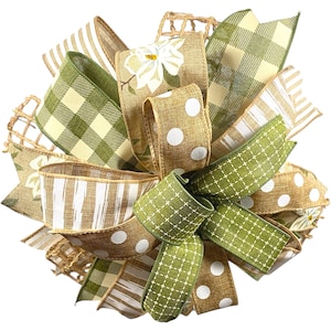 May include: A decorative bow featuring various patterned ribbons in shades of green, beige, and white. The bow includes ribbons with gingham, polka dots, and floral patterns, creating a layered and textured appearance. The bow is likely for seasonal or holiday decor.