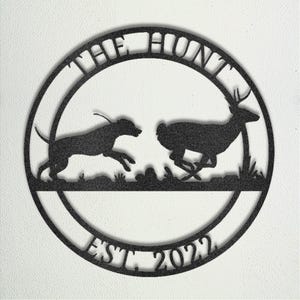 May include: A circular black metal wall sign featuring a silhouette of a hunting dog chasing a deer across a grassy field. The text THE HUNT is arched along the top inner border, and the text EST. 2022 is arched along the bottom inner border.