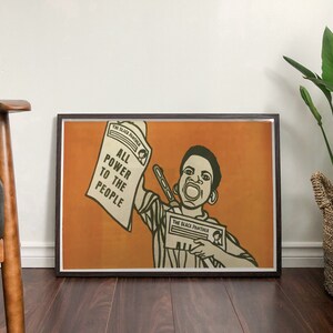 May include: A framed poster with an orange background featuring a young Black man holding a newspaper that reads "The Black Panther" and "All Power to the People".