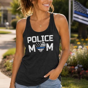 May include: A charcoal gray racerback tank top featuring the white distressed text POLICE MOM with a heart-shaped American flag graphic in the center, which includes a single horizontal blue stripe across the middle of the flag design.