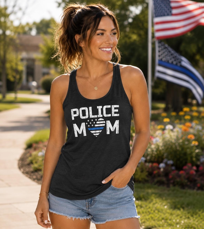 May include: A charcoal gray racerback tank top featuring the white distressed text POLICE MOM with a heart-shaped American flag graphic in the center, which includes a single horizontal blue stripe across the middle of the flag design.