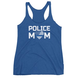May include: A royal blue racerback tank top featuring the white distressed text POLICE MOM. The letter O in MOM is replaced by a heart shape containing white stars and a horizontal blue line, mimicking a stylized American flag design.