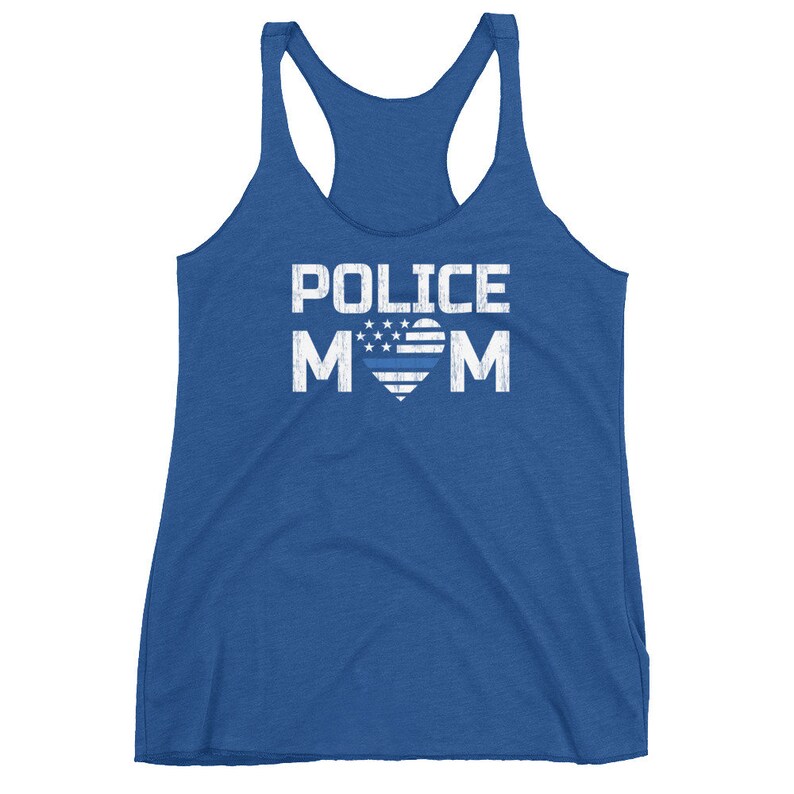 May include: A royal blue racerback tank top featuring the white distressed text POLICE MOM. The letter O in MOM is replaced by a heart shape containing white stars and a horizontal blue line, mimicking a stylized American flag design.