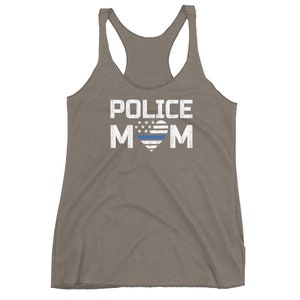 May include: A heathered brown racerback tank top featuring the white distressed text POLICE MOM. The letter O is replaced by a heart shape containing a white and blue American flag pattern with a horizontal blue line across the center of the heart.