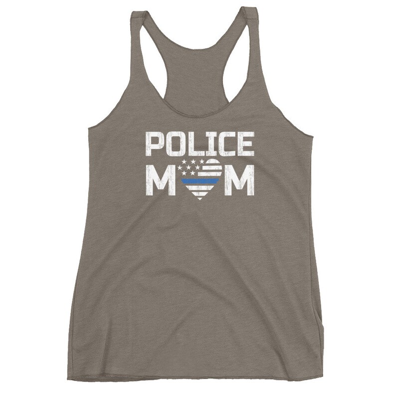 May include: A heathered brown racerback tank top featuring the white distressed text POLICE MOM. The letter O is replaced by a heart shape containing a white and blue American flag pattern with a horizontal blue line across the center of the heart.