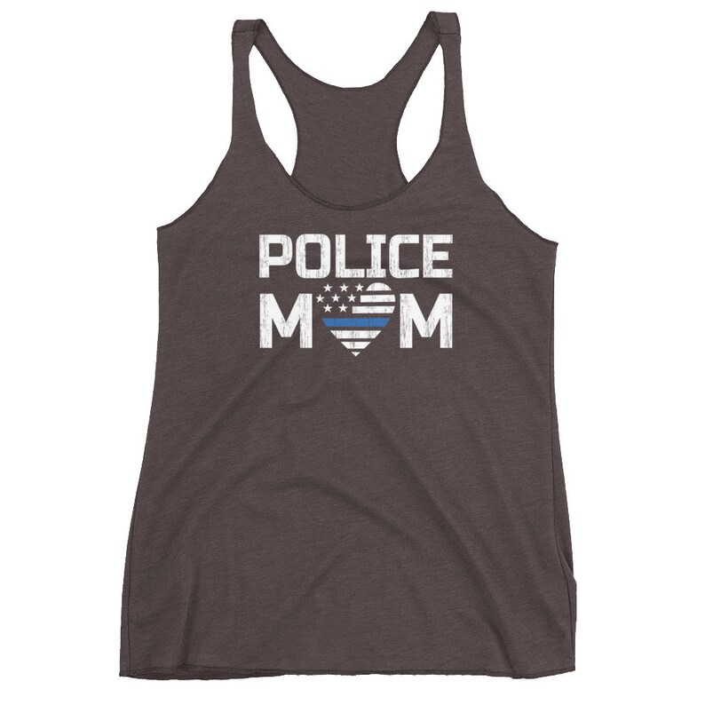 May include: A dark charcoal gray racerback tank top featuring the white text POLICE MOM printed on the front. The letter O in MOM is replaced by a heart shape containing a white and blue striped flag design with white stars on a blue field.