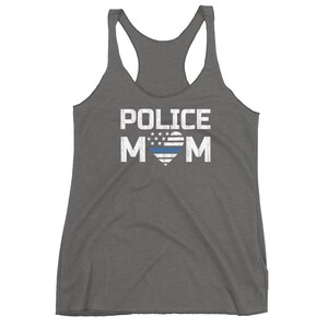 May include: A charcoal grey racerback tank top featuring the white distressed text POLICE MOM. The letter O is replaced by a heart shape containing a white star-spangled pattern and a single horizontal blue line across the center of the heart.