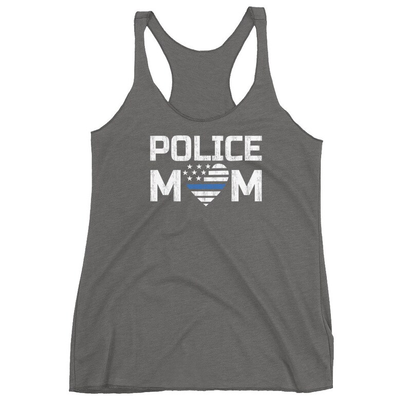 May include: A charcoal grey racerback tank top featuring the white distressed text POLICE MOM. The letter O is replaced by a heart shape containing a white star-spangled pattern and a single horizontal blue line across the center of the heart.