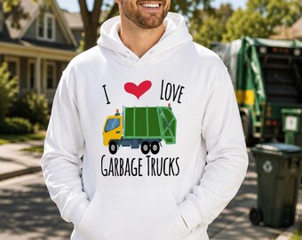 May include: A white hooded sweatshirt featuring a graphic print on the chest. The design includes the text "I LOVE GARBAGE TRUCKS" in black lettering with a red heart symbol and a yellow and green illustration of a garbage truck in the center.