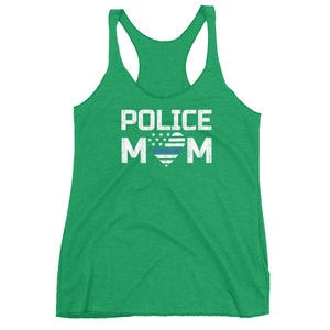 May include: A bright green racerback tank top featuring the white text POLICE MOM printed on the front. The letter O in MOM is replaced by a heart graphic containing white stars and stripes with a single horizontal blue line across the center.
