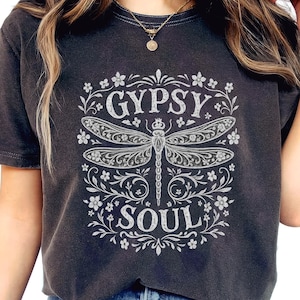 Puede incluir: Camiseta gris oscuro con un diseño de libélula y las palabras "GYPSY SOUL" en un marco floral. La camiseta se usa con vaqueros azules. La imagen también incluye el texto "PNG transparent background 300 (dpi)".